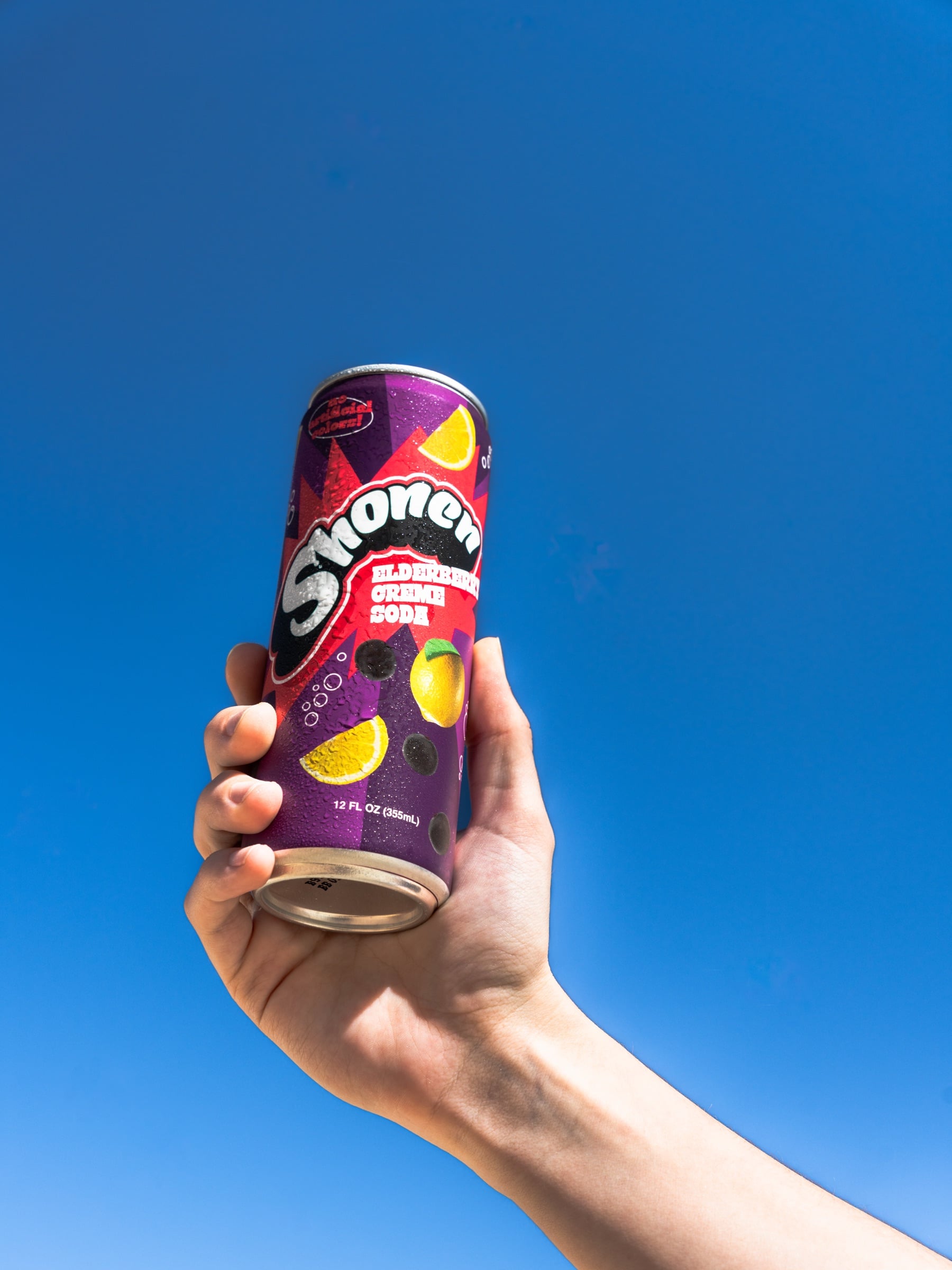 Hand holding a berry Shonen cream soda can against a clear blue sky