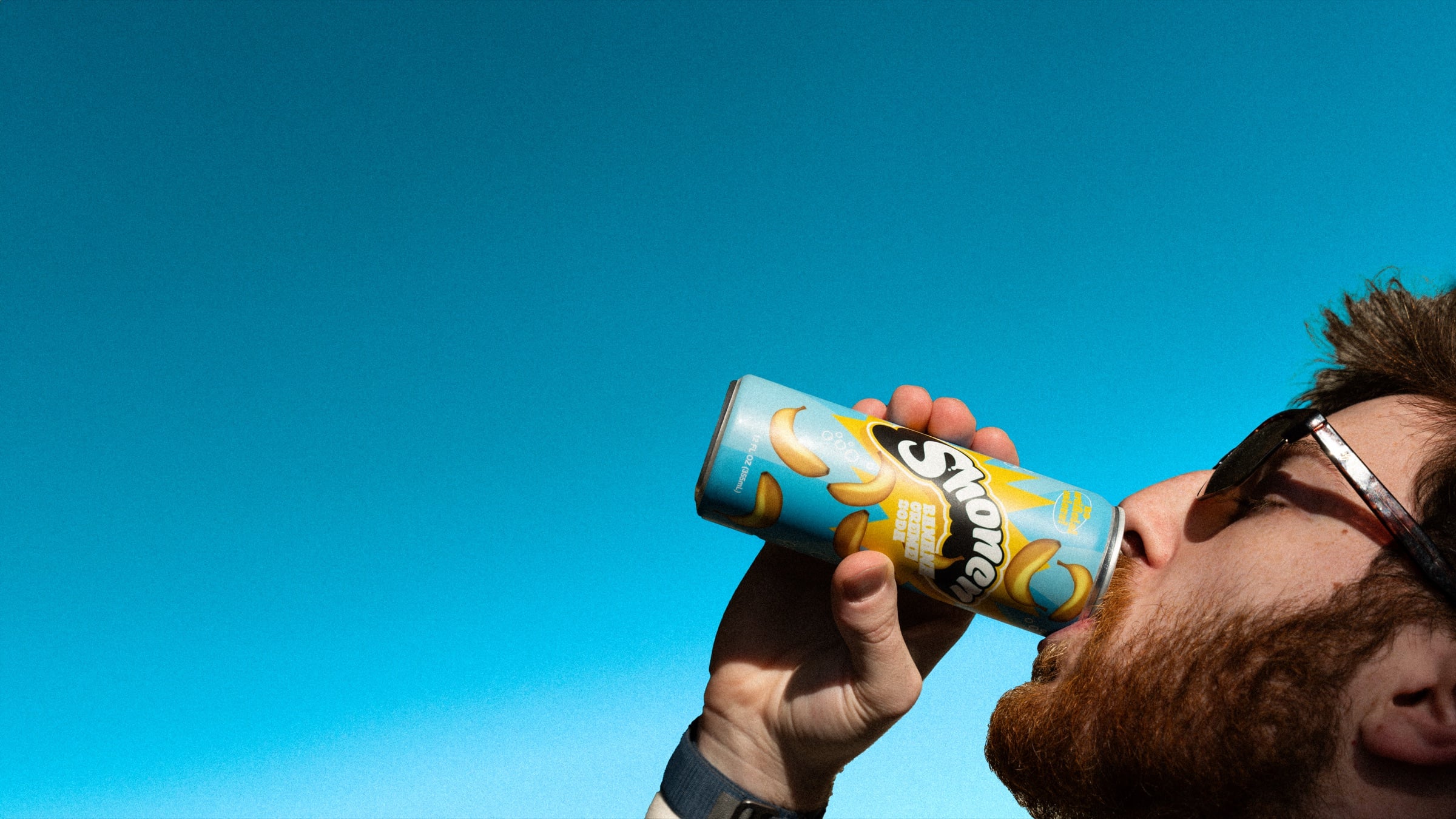 Man in sunglasses sipping a banana Shonen cream soda against a clear blue sky