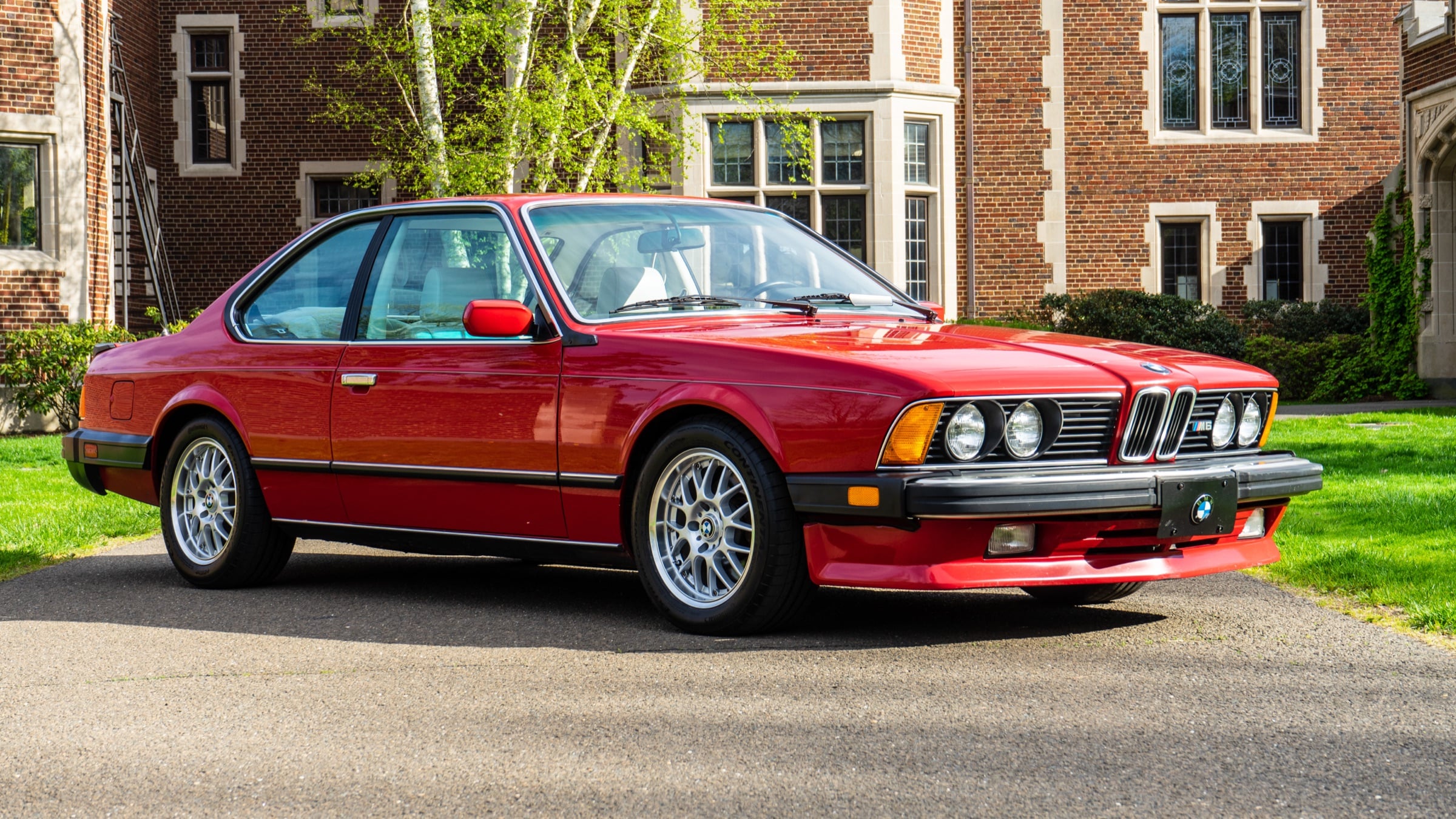 Red BMW E24 M6 coupe on an estate driveway, front three-quarter view