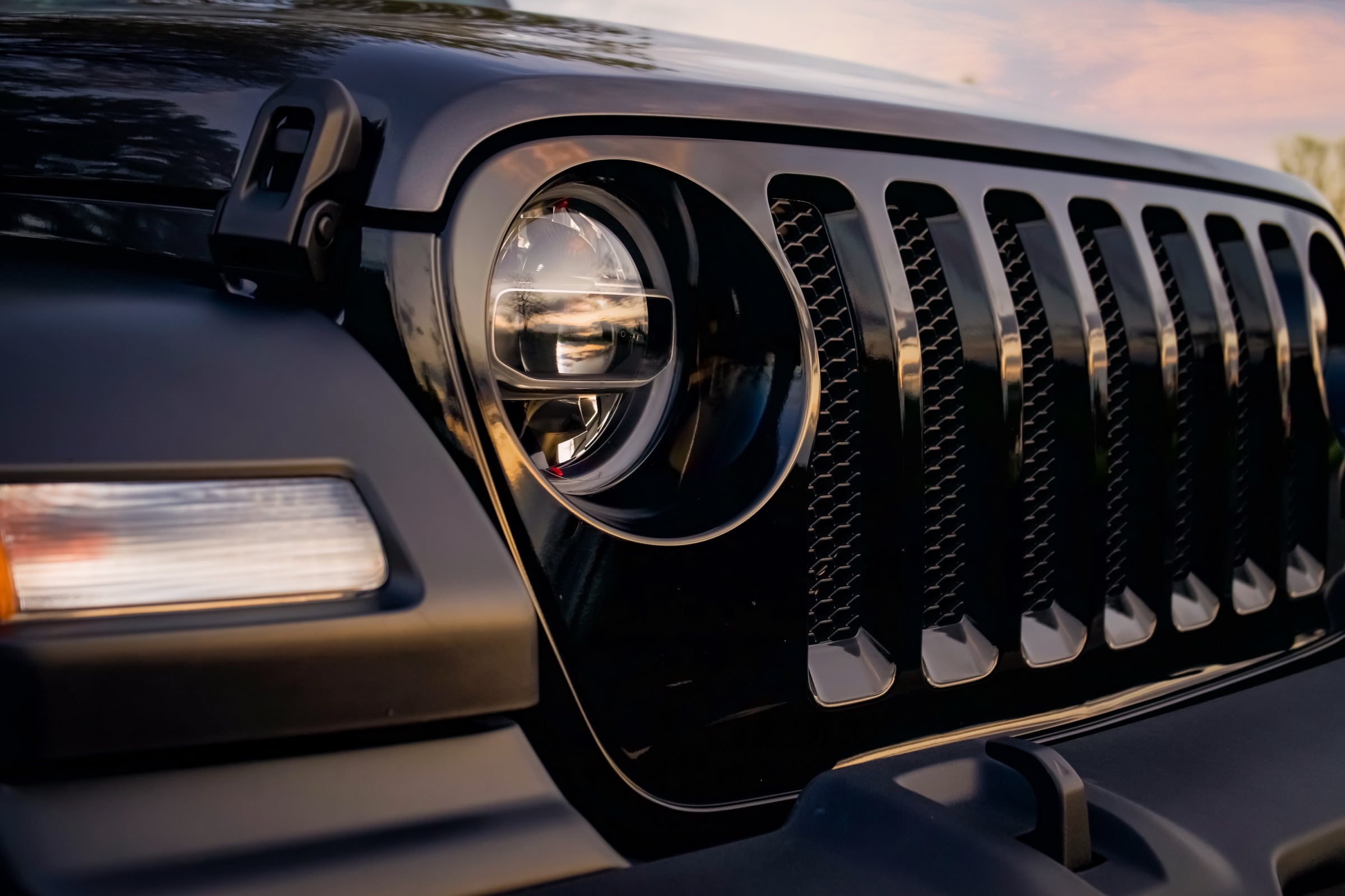 Close-up of a black Jeep Wrangler grille and round headlight at dusk