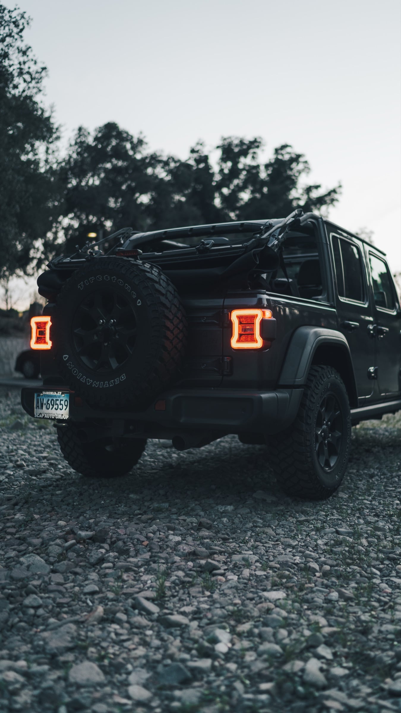 Rear three-quarter of a black Jeep Wrangler with glowing tail lights at dusk