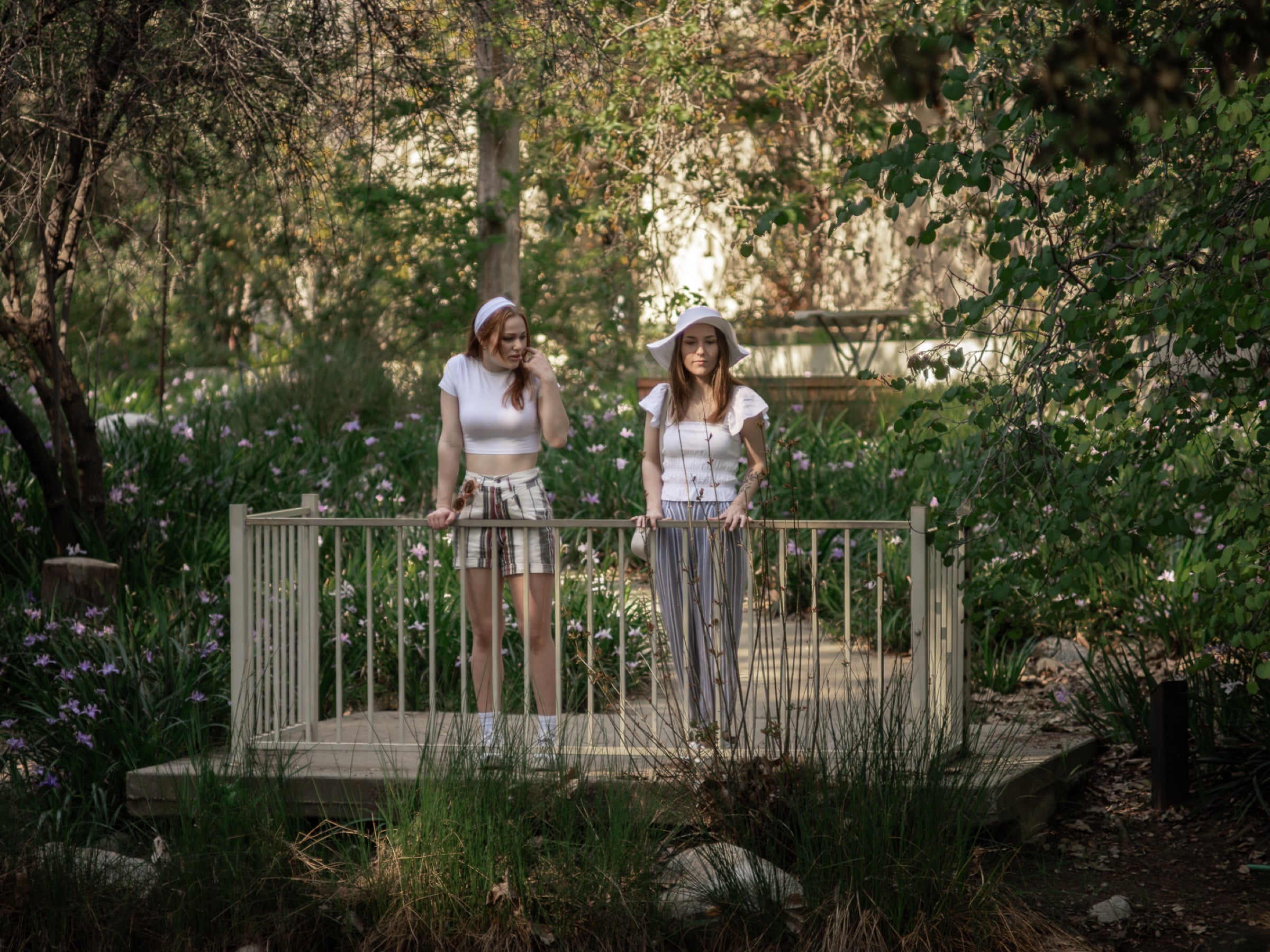Two women on a wooden footbridge in a lush flowering garden