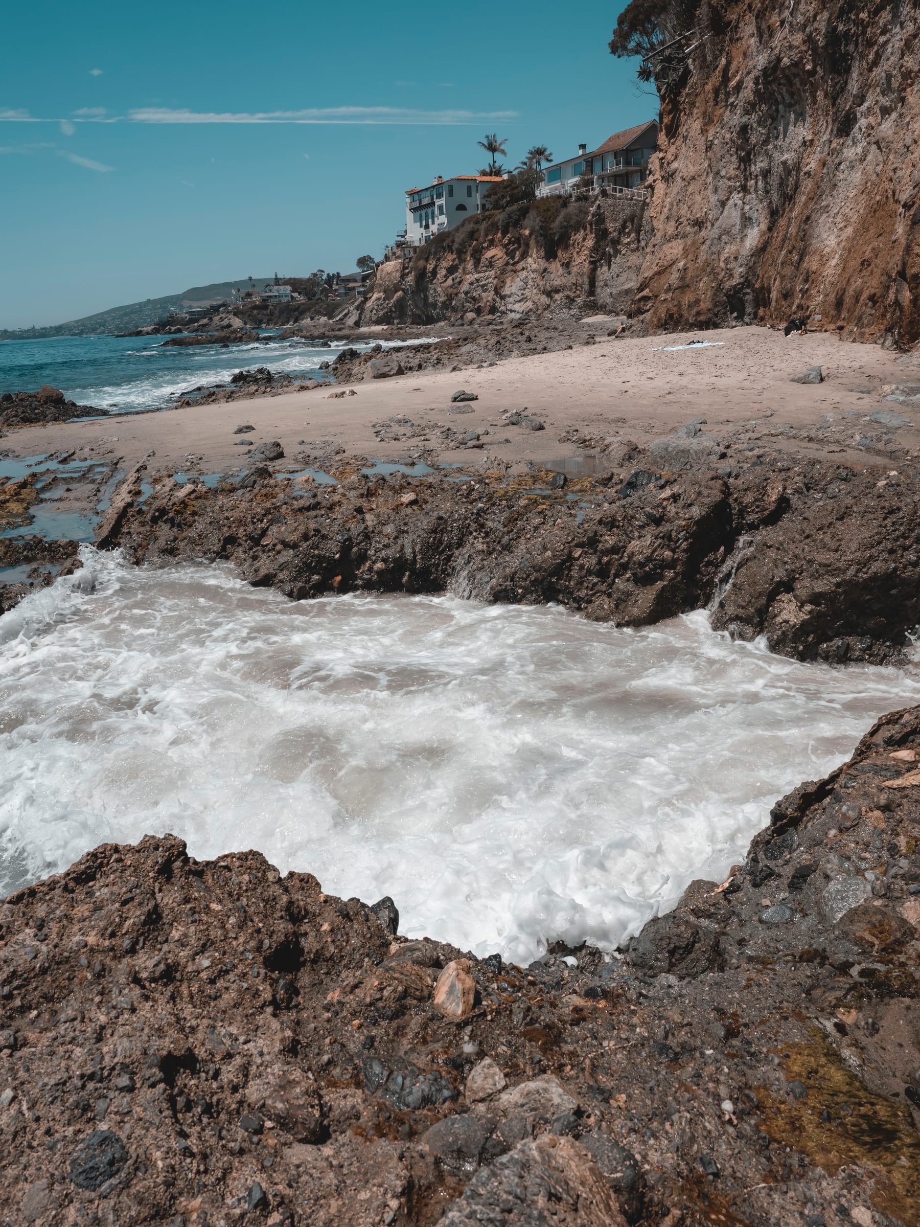 A wave rushing into a rocky cove below cliffside homes at Laguna