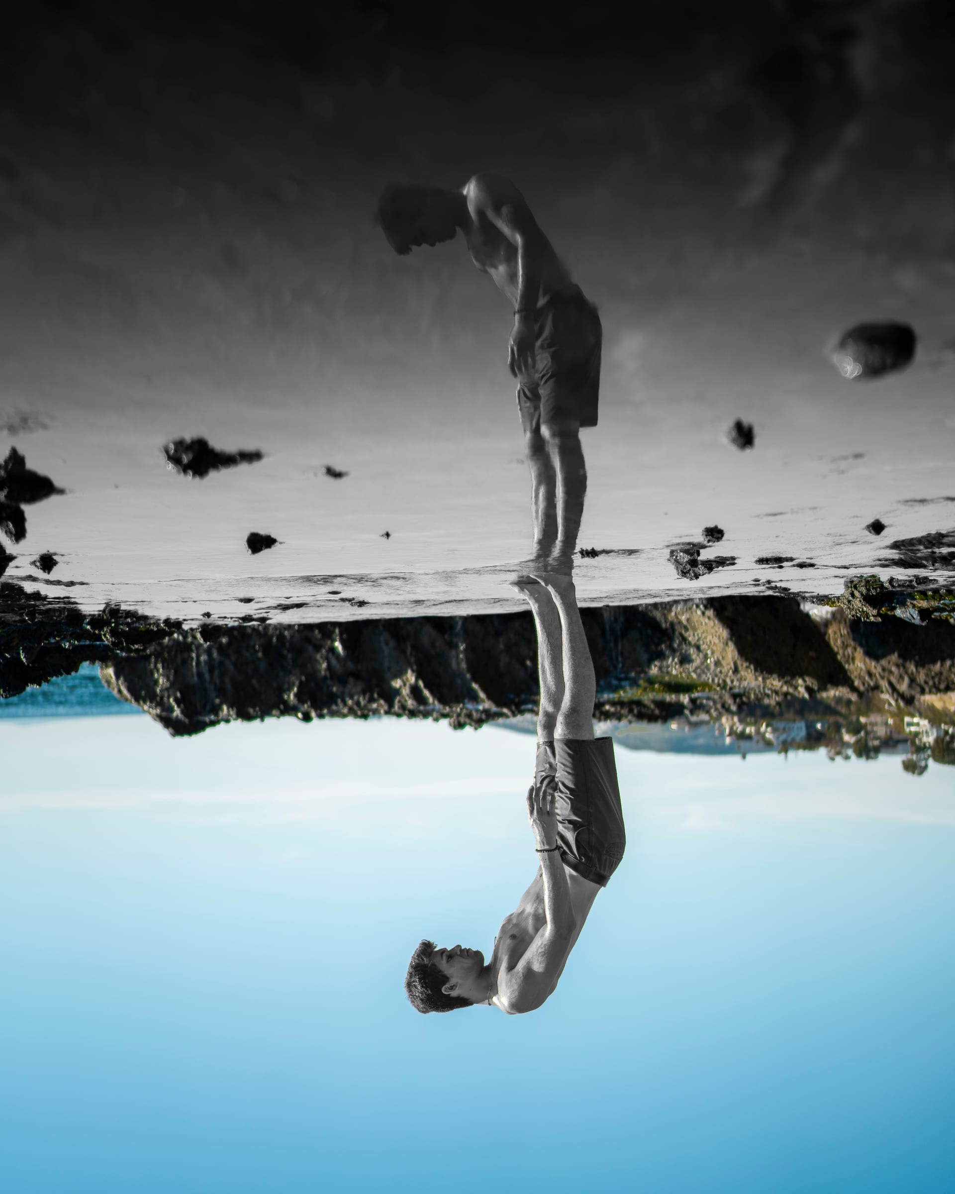 Inverted mirror reflection of a lone figure at the water's edge against a blue sky