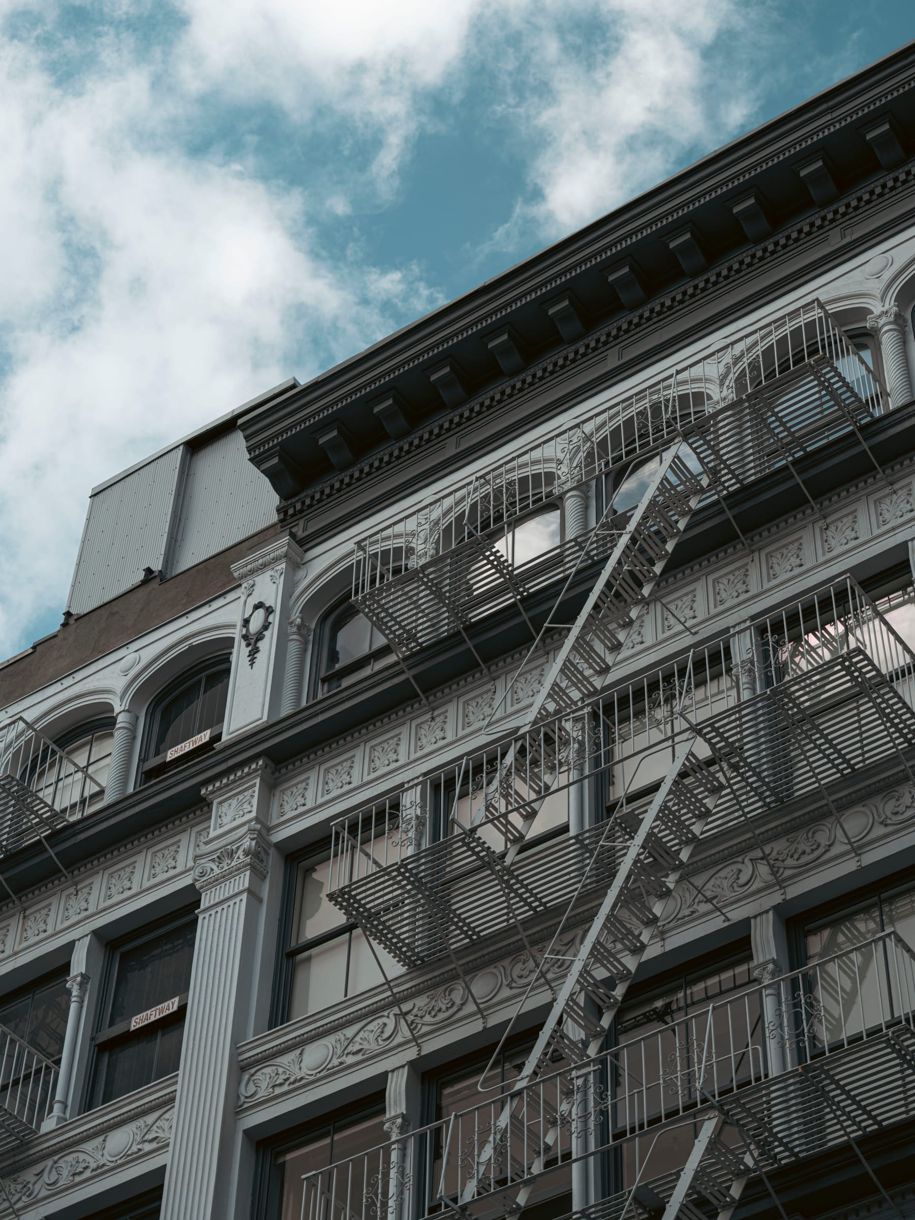 Ornate cast-iron facade and fire escape rising into a cloudy sky