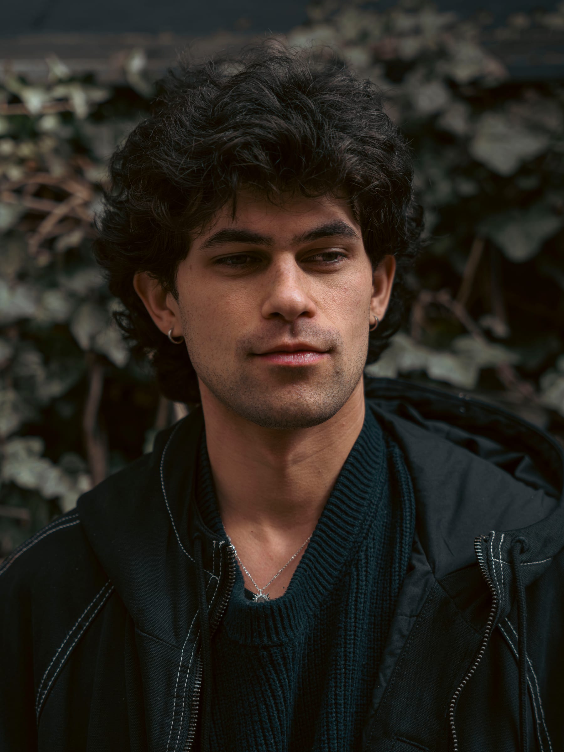 Editorial portrait of a young man with dark curls against ivy