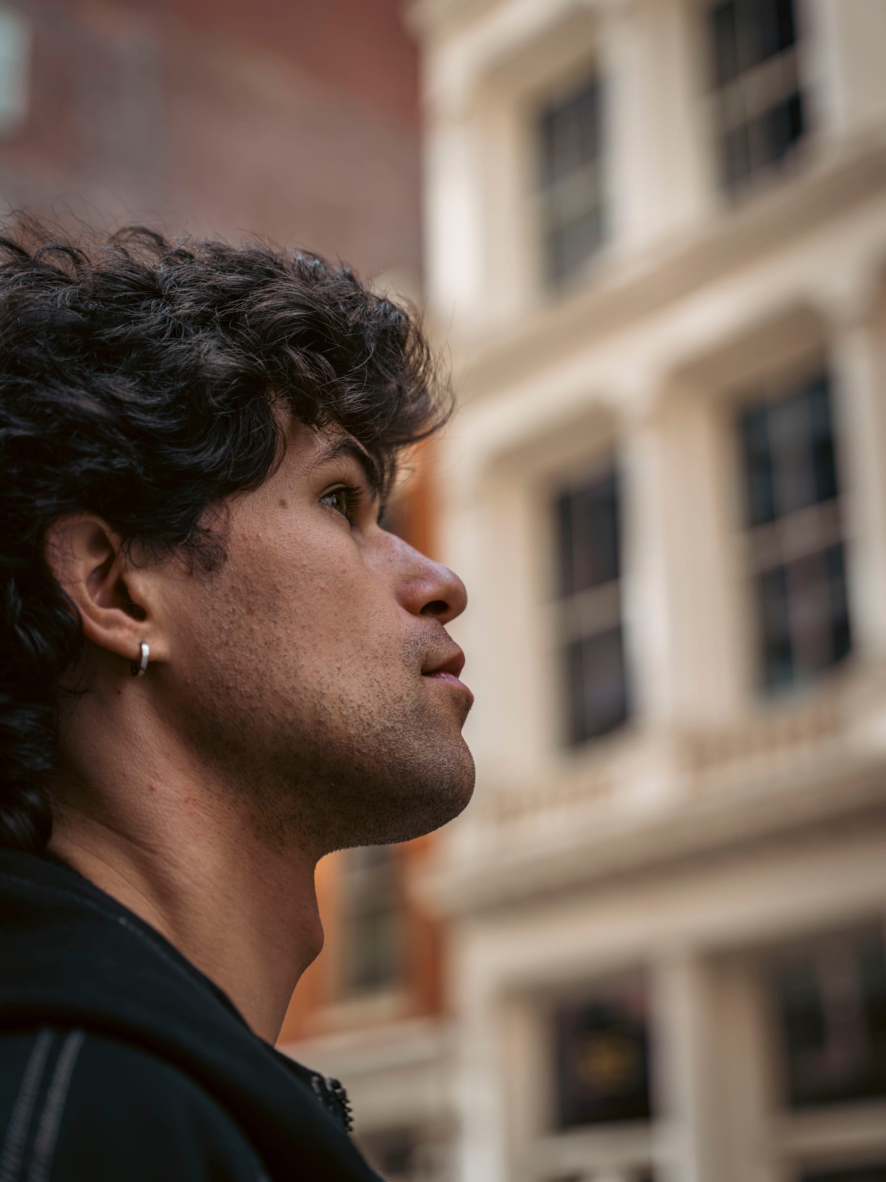 A young man in profile gazing upward, a sunlit pale facade rising behind him