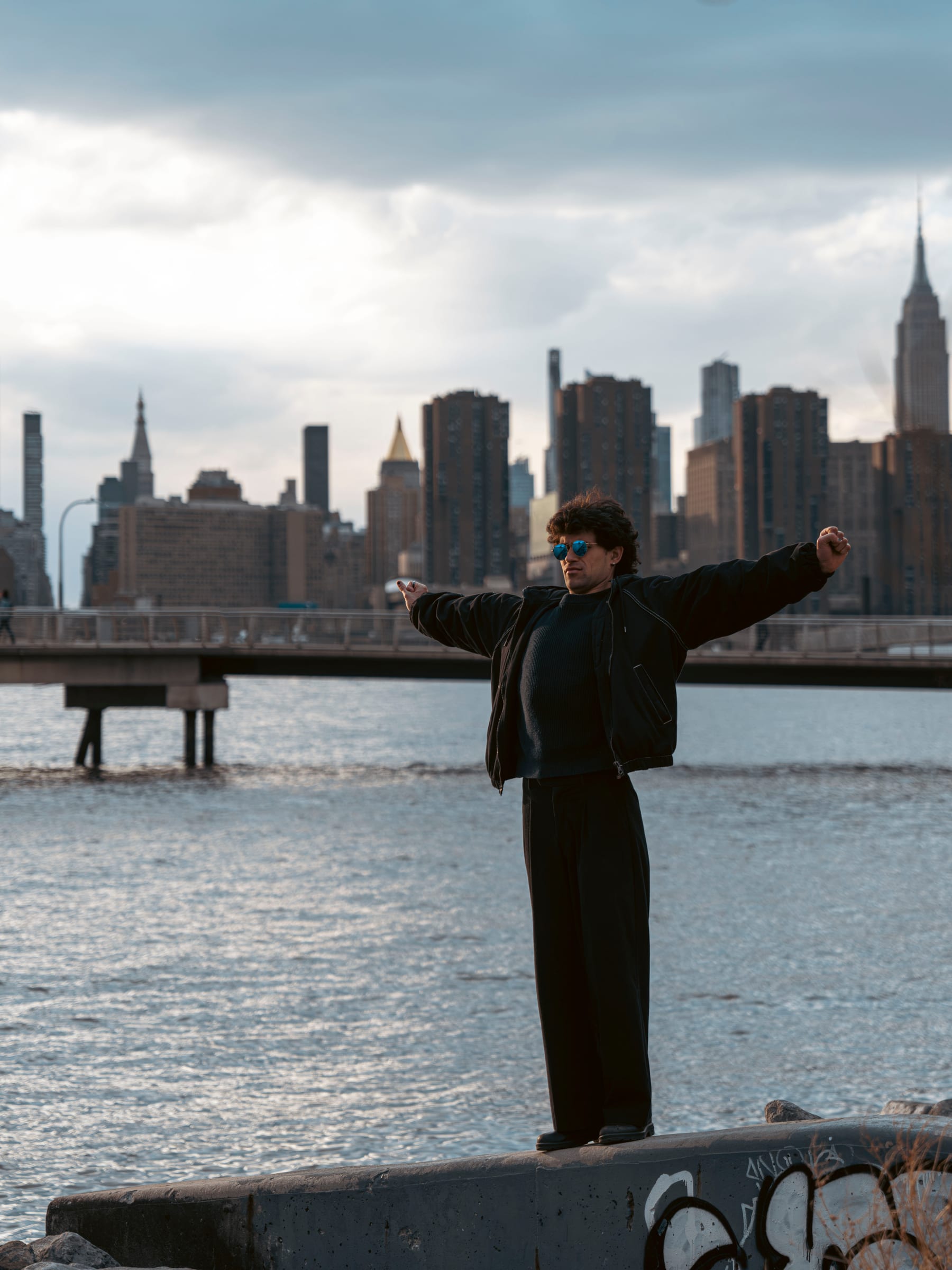 A man with arms outstretched before the Manhattan skyline at dusk