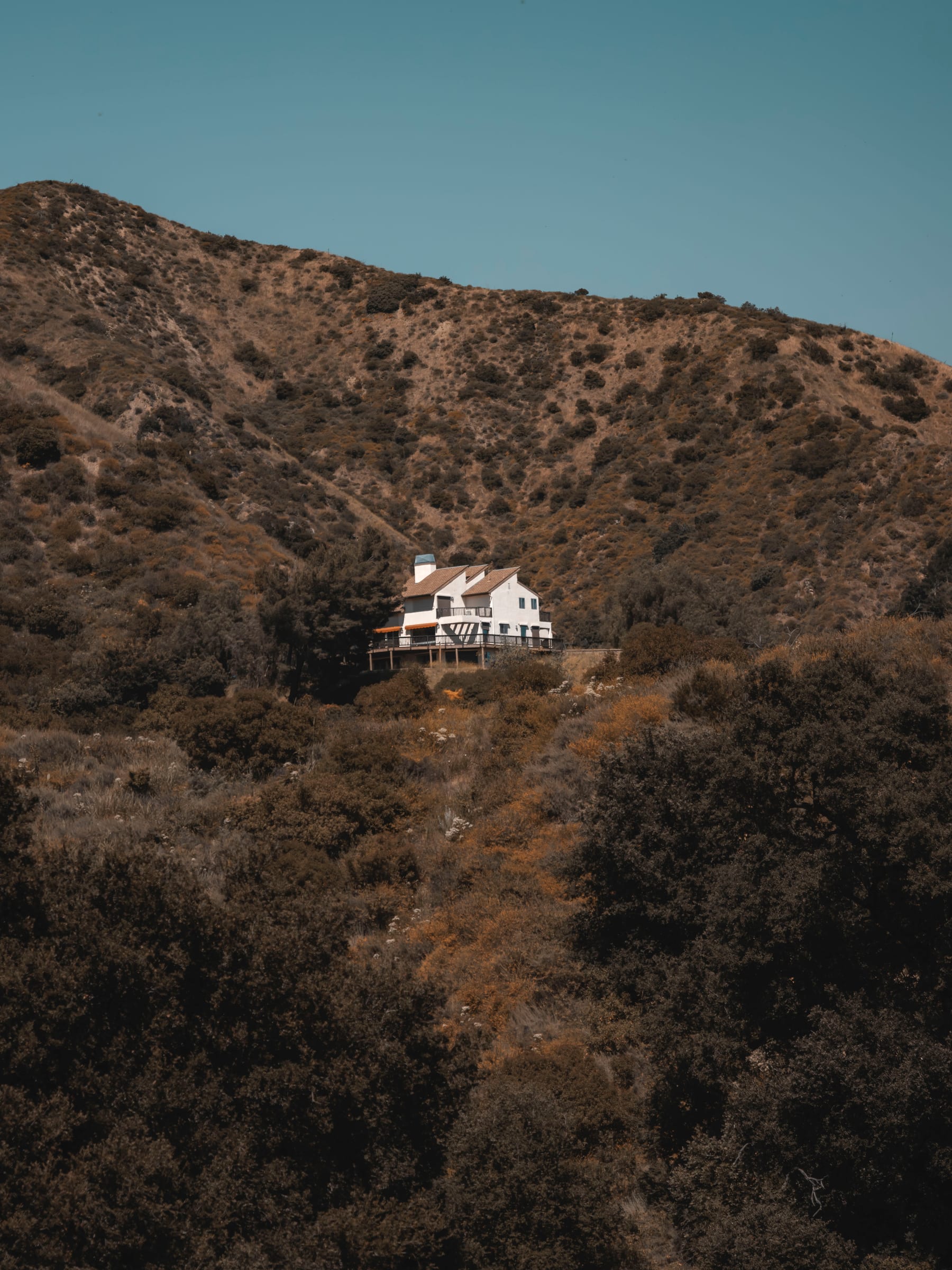 A lone house perched on a chaparral-covered hillside ridge