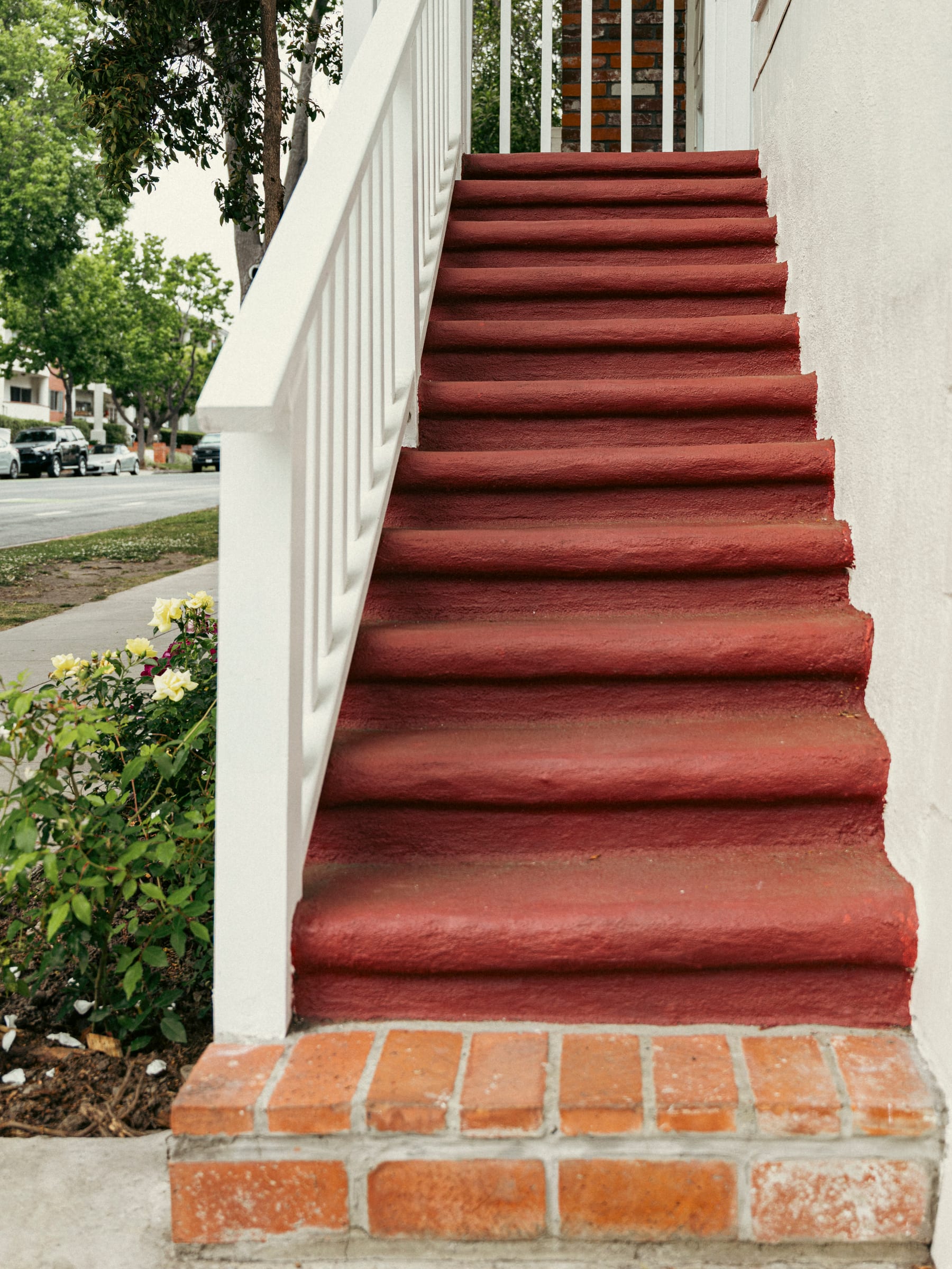Worn red-painted steps rising beside a white handrail and brick base