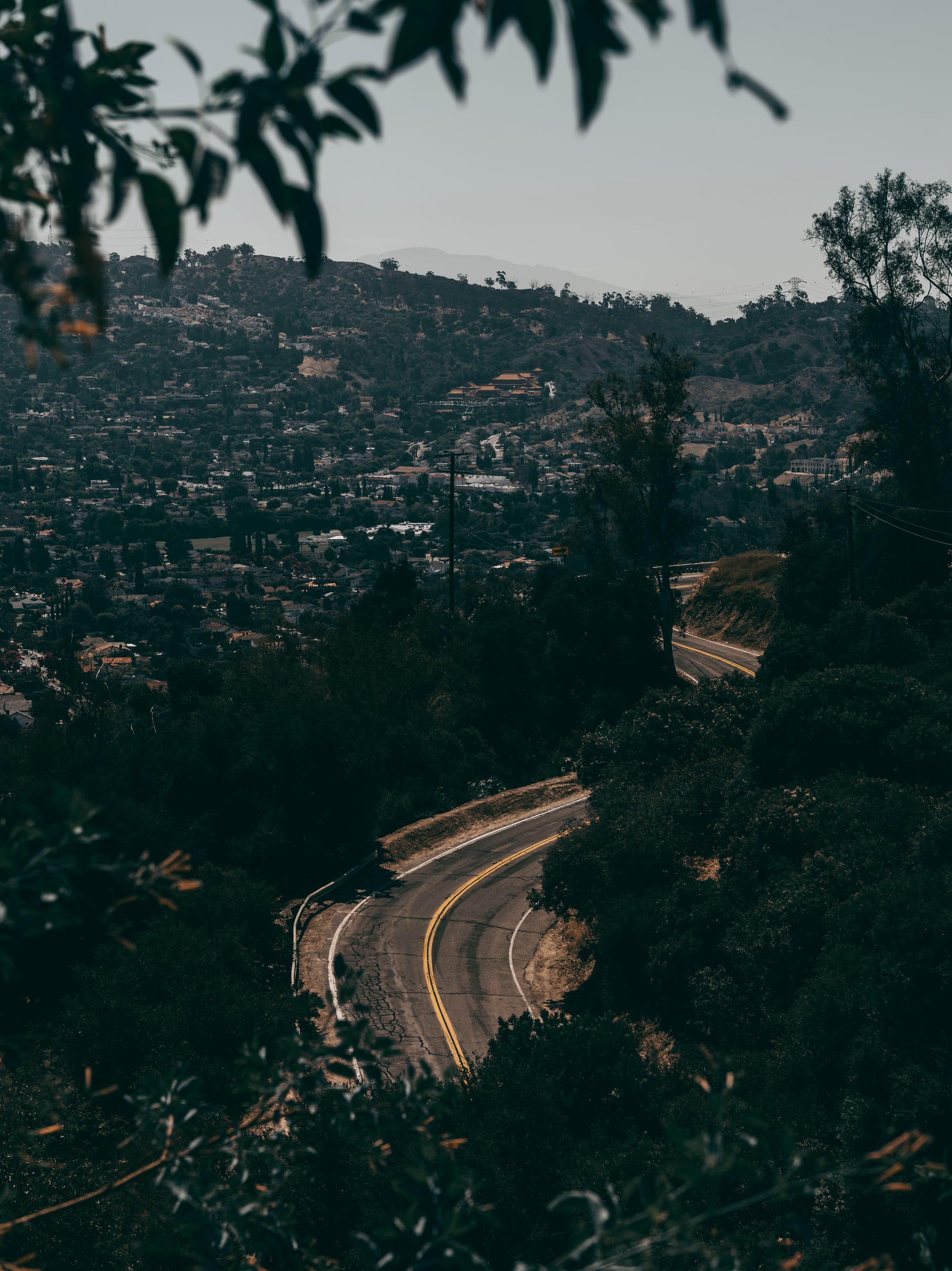 A road winding down through wooded hills above a hazy valley town