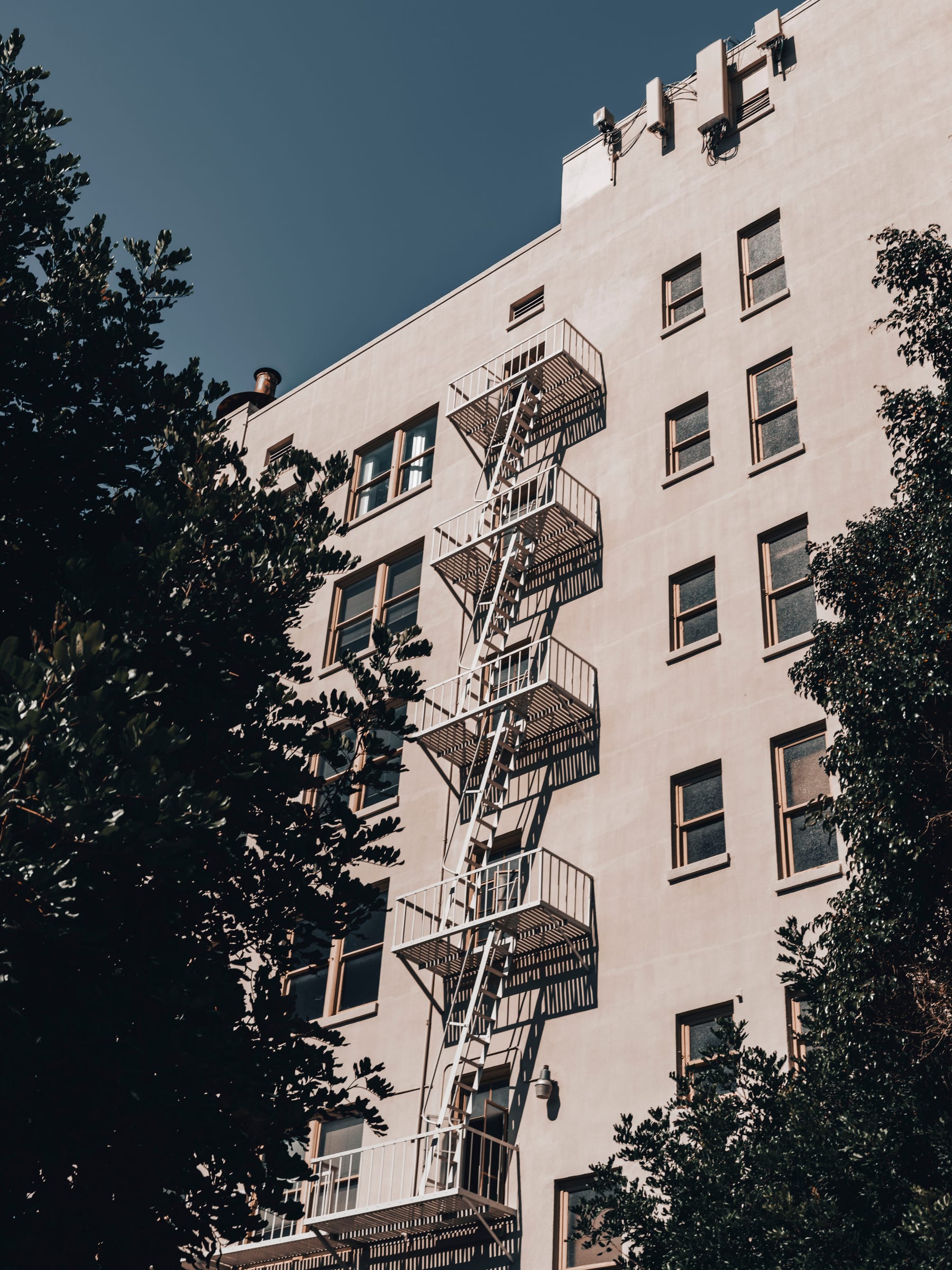 A zigzag fire escape climbing a white facade framed by trees