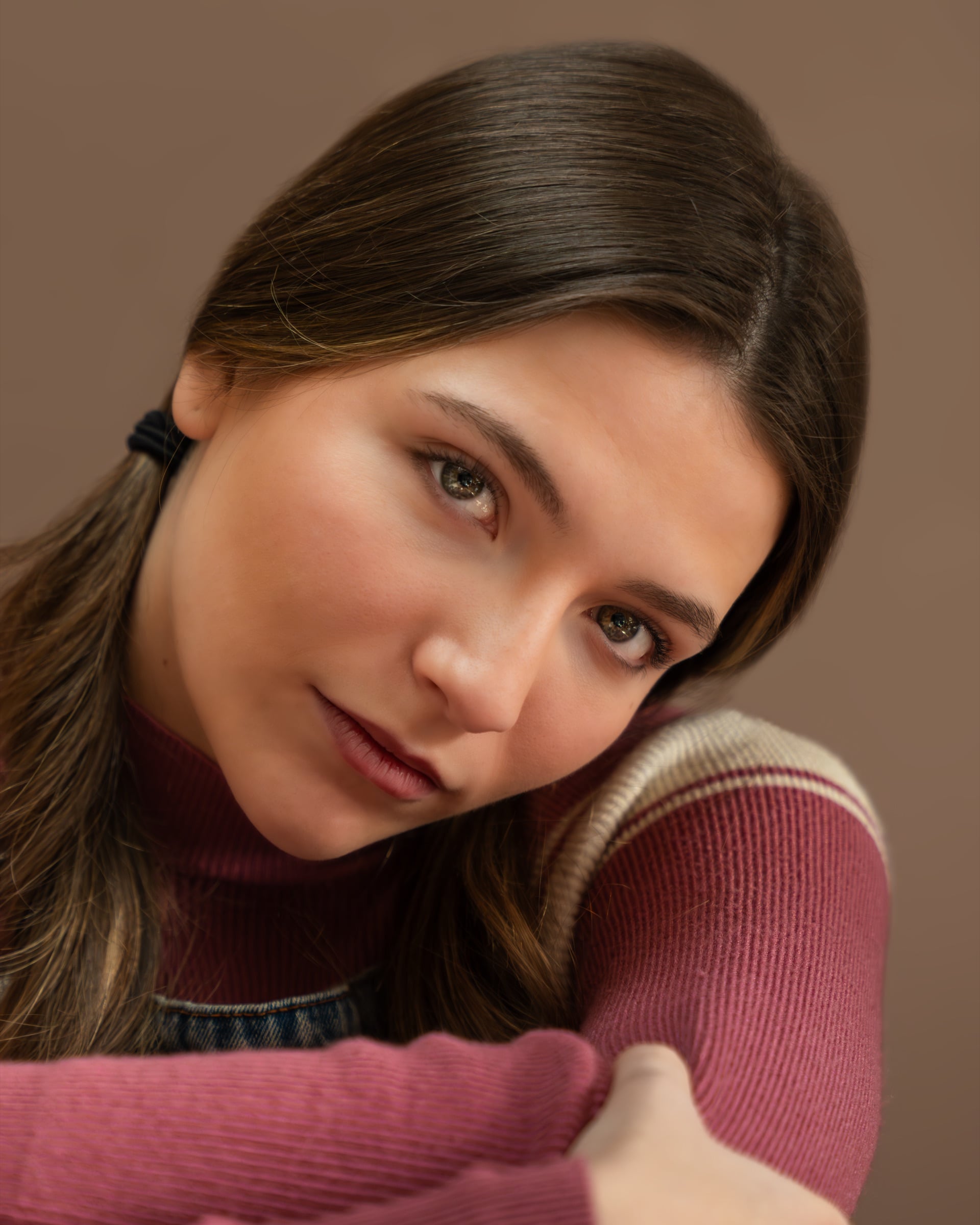 Studio headshot of a woman in a rose top leaning on her hand with a warm smile